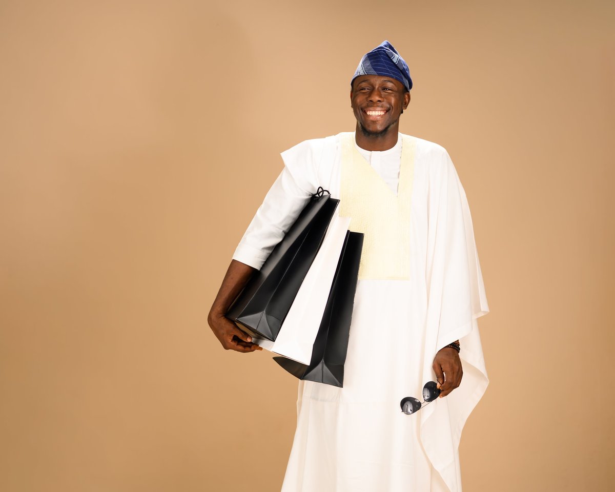 Joyful African man dressed in white agbada with a blue cap, smiling brightly in a studio setting