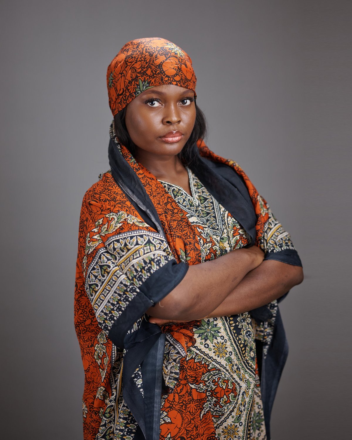 African woman wearing a patterned traditional dress and matching headscarf, looking calm and composed