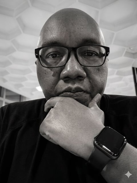 Black and white portrait of a man wearing glasses and a smartwatch, resting his chin on his hand in a thoughtful pose